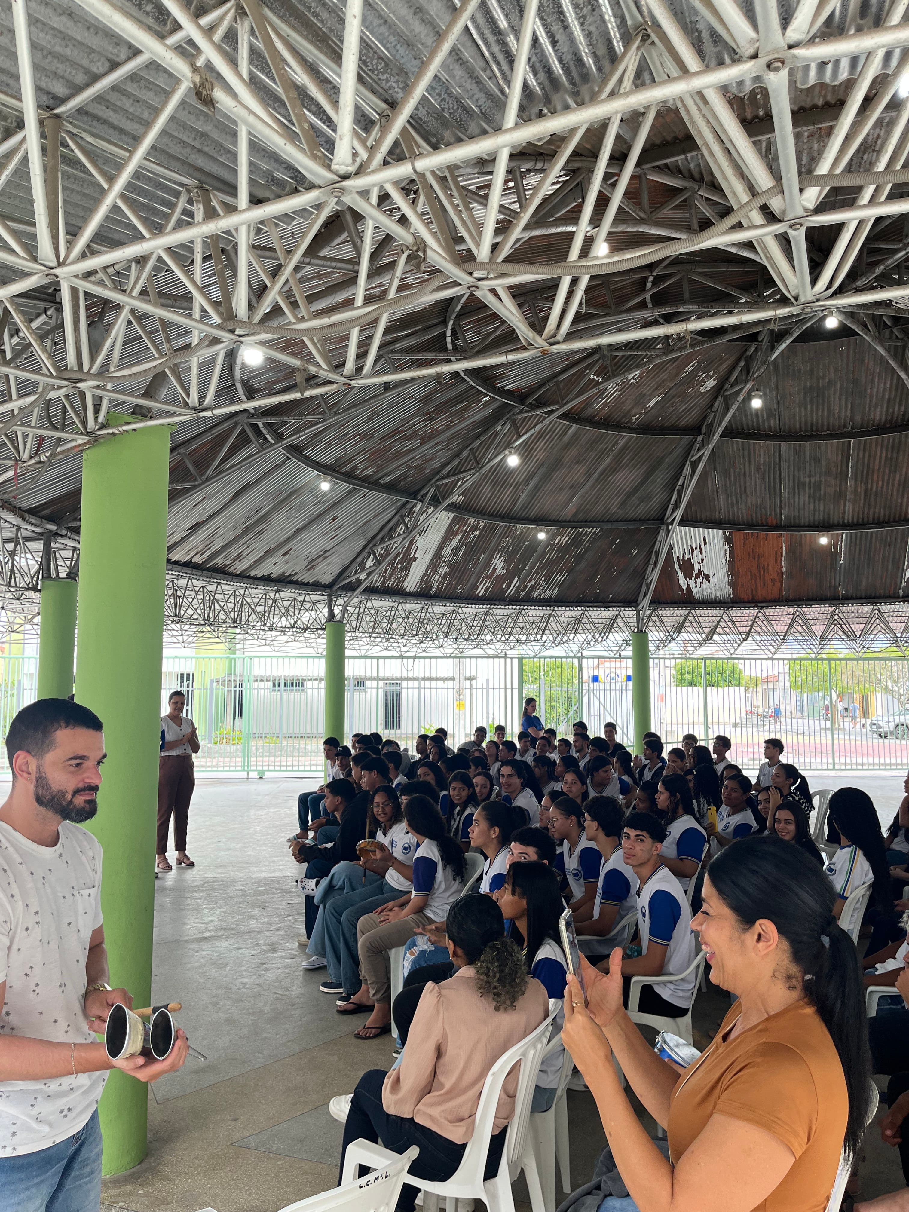 Vivência para todos: professor do colégio participa da oficina experimentando o ritmo no agogô.